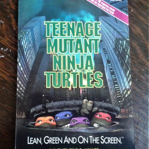 May include: A paperback book titled "Teenage Mutant Ninja Turtles" with a cityscape background. The cover features the turtles' faces peeking out of a sewer, with the text "Lean, Green and on the Screen."