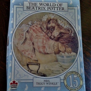 May include: A 15-piece round jigsaw puzzle featuring Mrs. Tiggy-Winkle from The World of Beatrix Potter. The puzzle shows a hedgehog wearing a red and white dress, holding a bowl and a spoon. The puzzle is on a blue background with white birds.