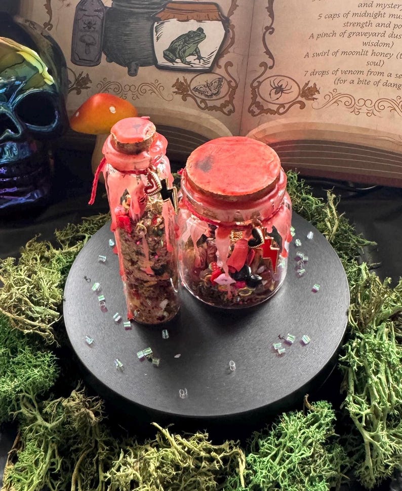 May include: Two glass containers with cork stoppers, one tall and one wide, filled with assorted small charms and beads. Both are sealed with red wax that drips down the sides. The containers feature small metal charms, including hearts and lightning bolts.