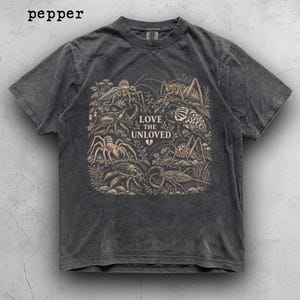 May include: A charcoal grey short-sleeve t-shirt with a vintage wash. The centre features a beige graphic illustration of various insects and arachnids surrounded by foliage. The text reads LOVE THE UNLOVED with a small broken heart icon below.