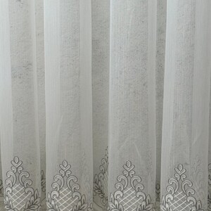 May include: Sheer white curtains with a delicate embroidered design along the bottom edge. The embroidery features a gray and white floral and geometric pattern. The curtains are made of a lightweight, semi-transparent fabric.