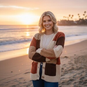 May include: A patchwork cardigan in shades of brown, beige, and orange. The sweater has a V-neck, long sleeves, and two front pockets. The cardigan is buttoned up and worn on a beach at sunset.