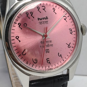 May include: A vintage wristwatch with a pink dial and silver hands. The watch face features Hindi numerals and text. It has a silver case and a black leather band. The watch is a classic timepiece.