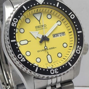 Peut inclure: Une tasse en céramique blanche avec une anse noire et le texte "But First, Coffee" en noir, dans une police manuscrite. La tasse est posée sur une surface blanche.