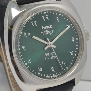 May include: Close-up of a silver wristwatch with a dark green face. The watch has silver hands and hour markers, and a black leather band. The watch face has text in a foreign language.
