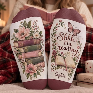 May include: A pair of white socks with dark red cuffs. The left sock features a stack of colorful books surrounded by pink and white flowers. The right sock displays a butterfly, an open book, the text Shhh I'm reading, and the name Sophia.