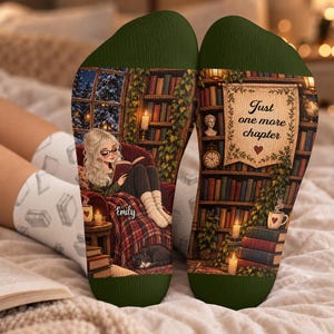 May include: A pair of dark green socks featuring a printed illustration of a person reading in a library setting. The design includes bookshelves, a cosy chair, a cat, and a banner with the text Just one more chapter and the name Emily.