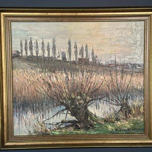 May include: An oil painting in a gold frame depicts a landscape with a body of water, trees, and tall grasses. The artwork has a muted colour palette with shades of brown, green, and grey. The painting is signed in the lower right corner.