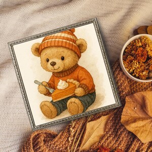 Puede incluir: Ilustración en acuarela enmarcada de un oso de peluche con un suéter y sombrero naranja, sosteniendo un tenedor con una rebanada de pastel de calabaza. El oso está sentado y la imagen tiene un tema otoñal.