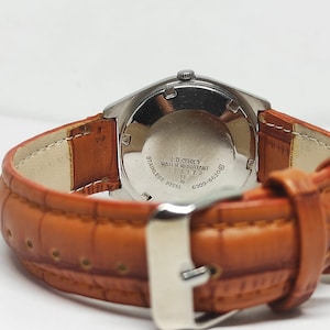 May include: Close-up of a vintage Seiko watch with a stainless steel case and a brown leather strap. The watch face is not visible, but the back of the watch shows text including "Stainless Steel" and "Water Resistant".