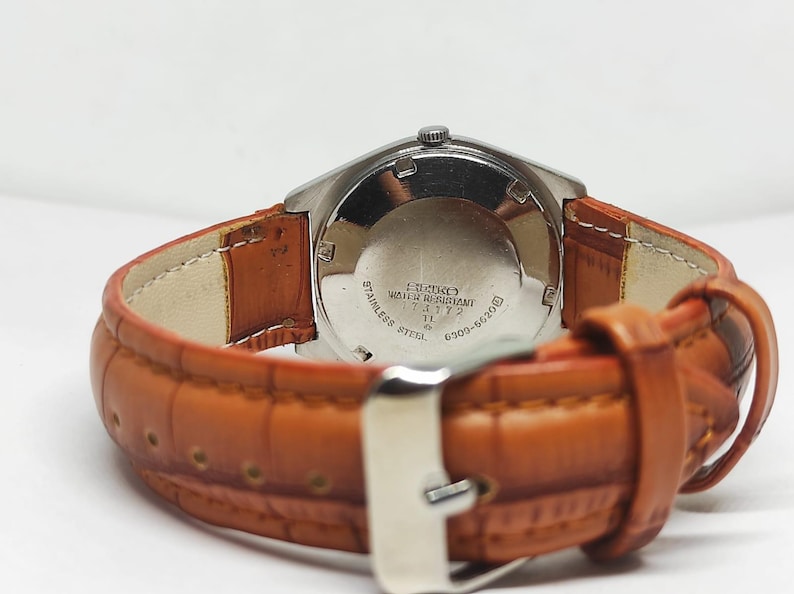 May include: Close-up of a vintage Seiko watch with a stainless steel case and a brown leather strap. The watch face is not visible, but the back of the watch shows text including "Stainless Steel" and "Water Resistant".
