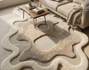 Puede incluir: Una alfombra de área abstracta y afelpada en tonos crema, beige y marrón claro. La alfombra presenta un diseño orgánico y fluido con texturas en capas y formas recortadas. El texto "INDIAN RUGS CLUB EST 2024" es visible.