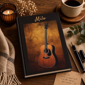 May include: A black hardcover journal featuring the name Milo in gold lettering at the top and a central graphic of an acoustic guitar against a textured brown background with a faint treble clef symbol. The cover has a smooth, matte finish.