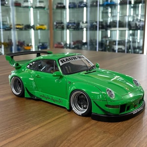 以下が含まれることがあります： ワイドボディキット、大型リアスポイラー、ブラックホイールを備えた明るいグリーンのスポーツカーのスケールモデル。フロントガラスにはRAUH-Weltの文字が表示され、サイドパネルにはRough Rhythmのスクリプトテキスト、フロントバンパーにはSekond Weltの文字が記されています。
