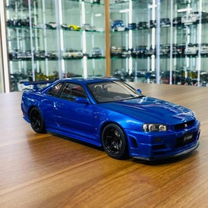 Könnte beinhalten: Ein blaues Sportwagen-Modell im Maßstab mit Heckspoiler, schwarzen Rädern und einem Emblem am Frontgrill. Das Fahrzeug hat eine aerodynamische Karosserie mit klaren Scheinwerfern und einem durch die Fenster sichtbaren, detaillierten Innenraum.