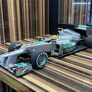 May include: A silver Mercedes-AMG Petronas Formula One scale model race car featuring black Pirelli P Zero tires, a yellow driver helmet, and sponsor decals including Petronas, MIG Bank, and Mercedes-Benz logos on the aerodynamic bodywork.