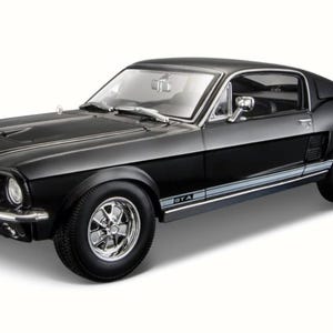 Może przedstawiać: Czarny model samochodu Ford Mustang fastback w skali, wyposażony w chromowane koła, srebrny pasek boczny z napisem GTA, przedni grill z emblematem kucyka oraz szczegółowe wnętrze widoczne przez przezroczyste szyby i przednią szybę.
