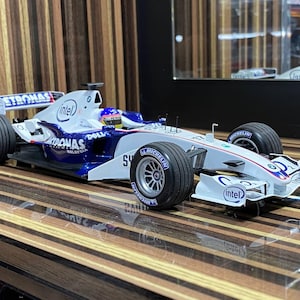 May include: A white and blue BMW Sauber F1 team scale model race car featuring Petronas, Intel, and Dell branding. The vehicle has black Michelin tires, a detailed cockpit with a driver figure, and aerodynamic wings on a sleek, low-profile body.