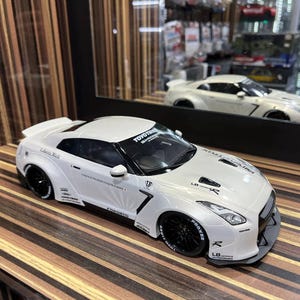 以下が含まれることがあります： 黒いホイール、ワイドボディキット、Toyo TiresやLiberty Walkなどのスポンサーデカールが施された白いスポーツカーのスケールモデル。黒いルーフ、スモークウィンドウ、リアスポイラーを備えています。