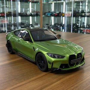 May include: A metallic lime green BMW M4 scale model car featuring black wheels, a black roof, and a front license plate that reads BMW M Performance Parts. The vehicle has a two-door coupe body style with detailed headlights and side mirrors.