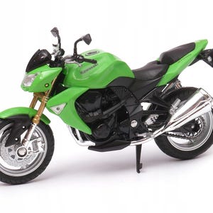 May include: A green and black Kawasaki Z1000 motorcycle model. The model features a green body, black accents, and silver exhaust pipes. The motorcycle has a black seat and gold-colored front forks. The Kawasaki logo is visible on the fuel tank.