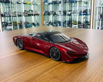 May include: A deep metallic red scale model sports car featuring a sleek aerodynamic body, a black roof, and black multi-spoke wheels. The vehicle has a low-profile design with sharp front headlights and a smooth, glossy finish on its exterior.