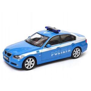 May include: A die-cast model of a blue and white BMW 330i police car. The car features the word "POLIZIA" in white lettering on the side, a blue light bar on the roof, and silver wheels. The model is set against a white background.