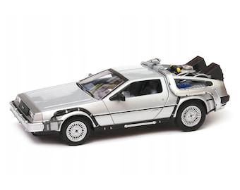 May include: Silver DeLorean model car with detailed features. The car has gull-wing doors, a futuristic design, and a detailed rear section with various components. The wheels are silver with white accents. The car is a collectible item.