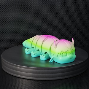 Puede incluir: Una figura de juguete colorida, con gradiente, de una criatura con un cuerpo segmentado, pequeños cuernos y cuatro pies. El juguete es principalmente verde, rosa y azul, y se exhibe en una plataforma circular negra.