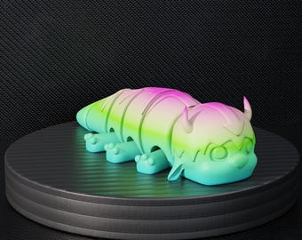 May include: A colorful, gradient-colored toy figure of a creature with a segmented body, small horns, and four feet. The toy is primarily green, pink, and blue, and is displayed on a black, circular platform.