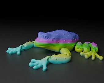 May include: A brightly coloured frog toy with a textured back in shades of purple, pink, and blue. The frog's belly transitions from yellow to green, with blue and green limbs. The frog is lying on a dark grey surface.