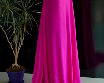 May include: A vibrant fuchsia fabric draped over a mannequin. The fabric cascades to the floor, creating soft folds and a flowing effect. A potted plant is in the background. The fabric is a solid color and appears to be lightweight.