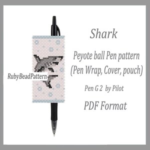 May include: A black pen with a beaded pen wrap featuring a shark design. The pen wrap is light pink with a pattern of small blue shapes and a grey shark illustration. Text on the image reads "Shark" and "Peyote ball Pen pattern".