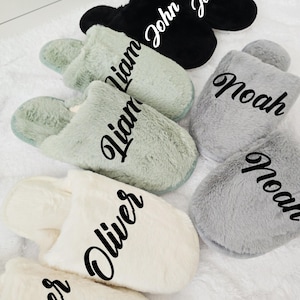 Flat lay display of cozy personalized men's slippers in black, grey, mint, and cream colors with custom names — Liam, John, Noah, and Oliver.