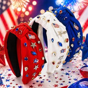 May include: Three patriotic headbands in red, white, and blue. Each headband is adorned with sparkling gemstones, star-shaped embellishments, and miniature American flags. The headbands are knotted at the top and are perfect for celebrating patriotic holidays.