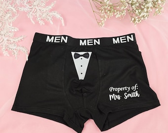 May include: Black boxer briefs featuring a white waistband with the repeated text MEN. The front displays a white tuxedo shirt front graphic with a black bow tie and three buttons. The text Property of: Mrs. Smith is printed in white on the leg.