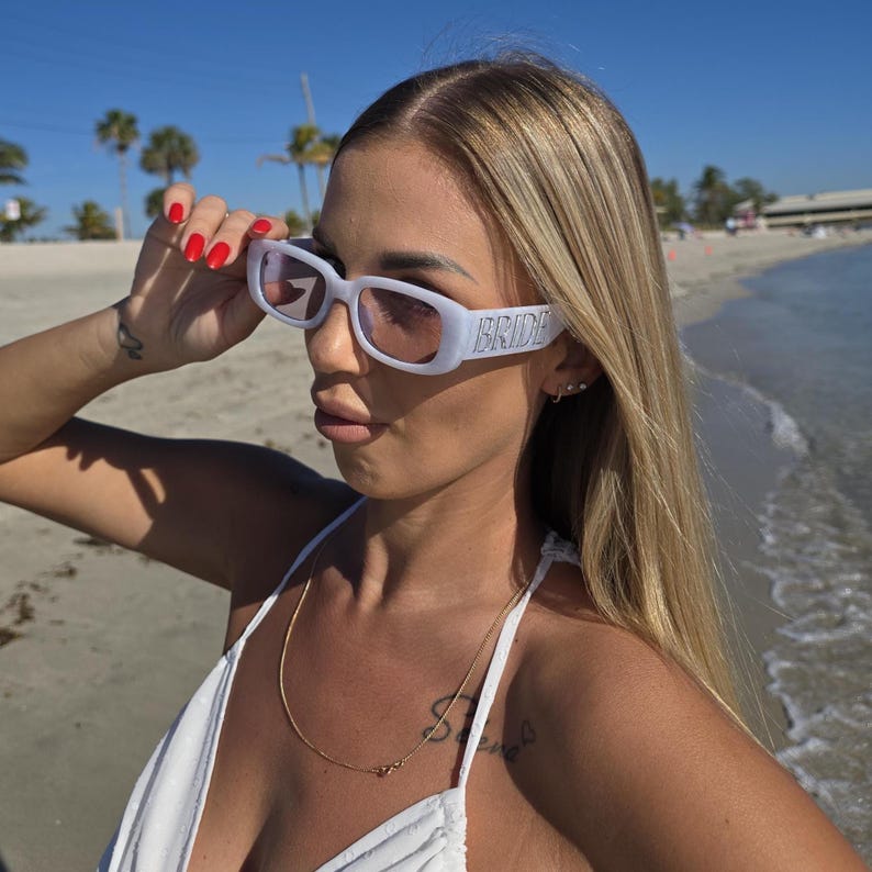 Bride-to-be white sunglasses with custom “BRIDE” side detail, trendy rectangular bridal eyewear, beach honeymoon accessory, bridal shower sunglasses, fashionable bride beach look for vacation and wedding festivities.