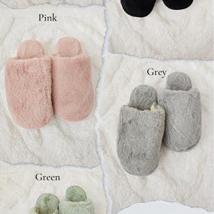 Four pairs of fuzzy closed slippers in different colors – white, black, pink, and green – displayed on a soft white background with text labels showing each color option, from GT Boutique Shop.