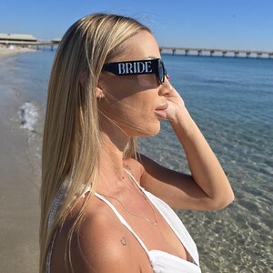 Black bride sunglasses with bold “BRIDE” text, bridal party sunglasses for bride-to-be, chic wedding weekend eyewear, honeymoon beach sunglasses, modern bridal accessory for bachelorette celebration and destination wedding.