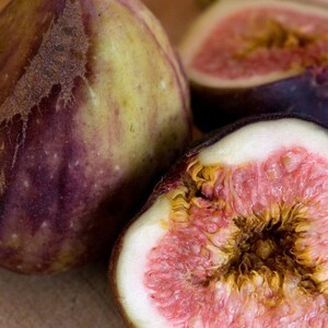 May include: Three whole figs, two are cut in half, revealing the pink flesh and dark seeds inside. The figs are a deep purple color with a green tinge.