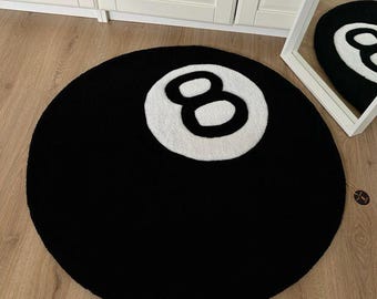 May include: A circular black rug featuring a white number eight, mimicking an eight ball. The rug is placed on a wooden floor. A mirror reflects the rug's design. The rug is a decorative item, likely for a home.