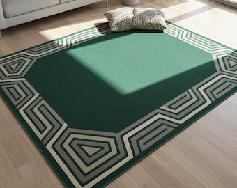 May include: A rectangular green area rug with a geometric border in shades of gray and off-white. The rug is placed on a hardwood floor, with a sofa and pillows visible in the background. The rug's design features angular shapes.