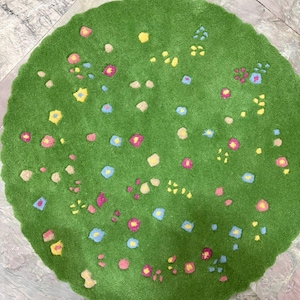 May include: A round, green rug with a floral design. The rug features a field of small, colorful flowers in shades of pink, yellow, blue, and beige. The rug's edge has a scalloped design.