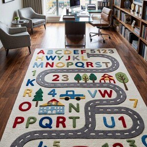 May include: A rectangular area rug featuring a cream-coloured background with a winding grey road pattern. The design includes colourful raised letters of the alphabet, numbers, and small icons of trees, buildings, and cars scattered across the surface.