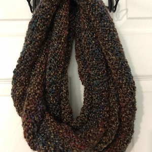 May include: A chunky knit infinity scarf featuring a variegated yarn blend of dark brown, deep blue, and subtle rust red tones. The scarf has a thick, textured stitch pattern and is formed into a continuous loop, creating a voluminous circular shape.