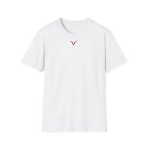 Può includere: T-shirt bianco a maniche corte con un piccolo emblema rosso centrato sul petto. L'emblema è un design stilizzato e astratto. La maglietta è realizzata in un tessuto liscio e semplice.