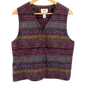 May include: A sleeveless waistcoat featuring a multi-coloured horizontal striped pattern in shades of purple, blue, and olive green. The garment includes a V-neckline, a front button closure with four matching fabric-covered buttons, and a paisley print.