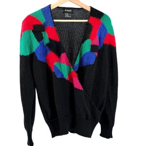 May include: A black long-sleeve sweater featuring a V-neckline and a wrap-style front. The upper chest and shoulders are decorated with a geometric pattern of red, blue, and green blocks. The interior label displays the brand name IMARI.
