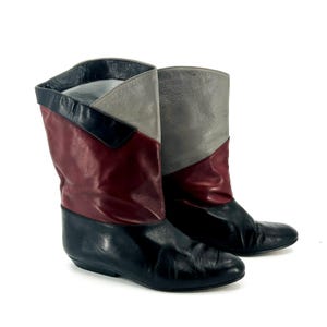 May include: A pair of vintage leather boots. The boots feature a color-blocked design with black, burgundy, and gray panels. The boots have a mid-calf height and a low heel. The boots are likely from the 1980s or early 1990s.