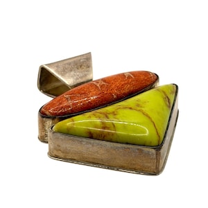 May include: A pendant featuring a polished, triangular lime green stone and an elongated, oval-shaped reddish-orange stone set in a silver-toned metal frame. The piece includes a large, angled silver-toned bail for attachment to a necklace chain.